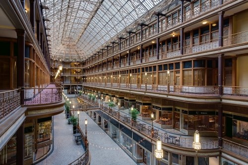 A spacious, historic atrium with glass ceilings, balconies, and shops lining the interior. Soft lighting enhances the ambiance.