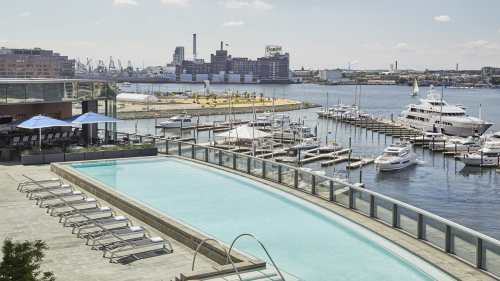 A serene pool overlooks a marina filled with boats, with a city skyline in the background under a clear blue sky.