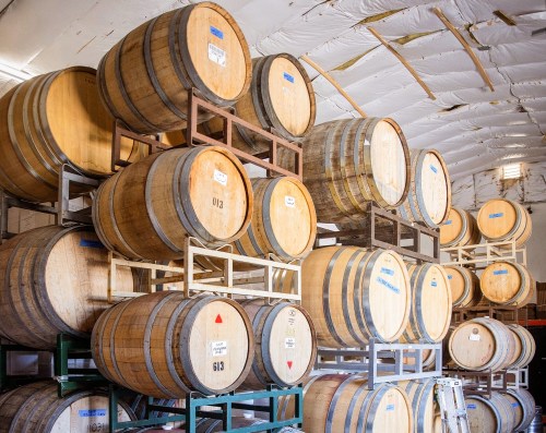 A stack of wooden barrels stored on racks inside a warehouse, with a white ceiling above.