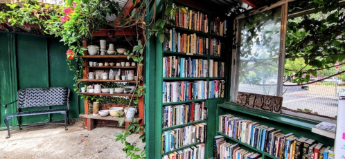 A cozy outdoor reading nook with bookshelves, plants, and a bench, creating a serene atmosphere for relaxation.