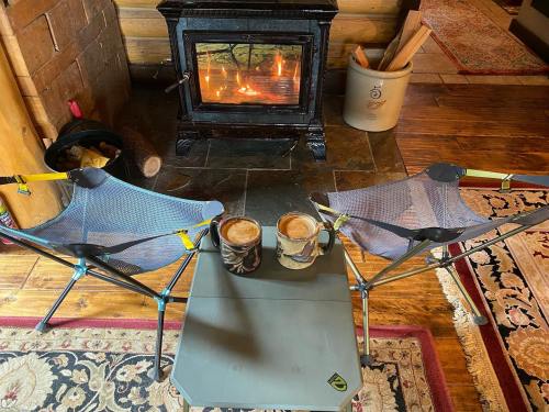 Two camping chairs facing a cozy fireplace, with two mugs of coffee on a small table in between.