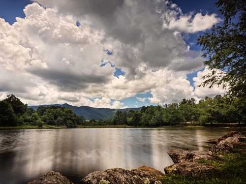 A serene lake surrounded by lush greenery and mountains, under a sky filled with fluffy clouds.