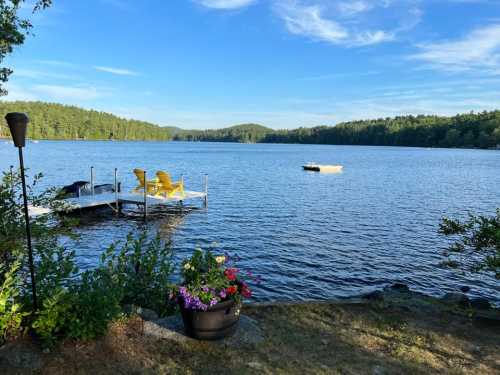 A serene lake view with a dock, yellow chairs, and lush greenery under a clear blue sky.