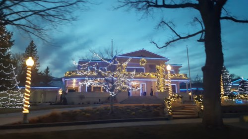 A beautifully lit building adorned with festive lights, surrounded by trees and a twilight sky.
