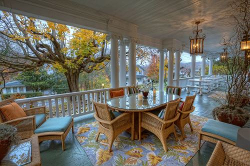 A cozy porch with wicker furniture, a round table, and autumn foliage in the background, creating a warm, inviting atmosphere.