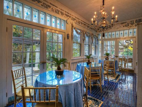 Bright sunroom with blue tables, gold chairs, and large windows, featuring plants and a chandelier.