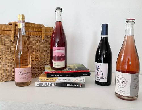 A picnic basket beside a selection of wine bottles and stacked books on a shelf.