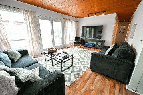 Cozy living room with dark sofas, a coffee table, and a large TV, featuring wooden ceiling and light curtains.