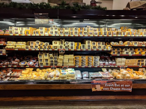 A well-stocked cheese display featuring various types and brands of cheese in a grocery store.