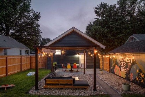 Cozy backyard with a covered seating area, string lights, and a mural reading "Midwest Does It Best" at dusk.