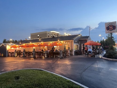 A cozy restaurant with outdoor seating, illuminated by string lights, during twilight.