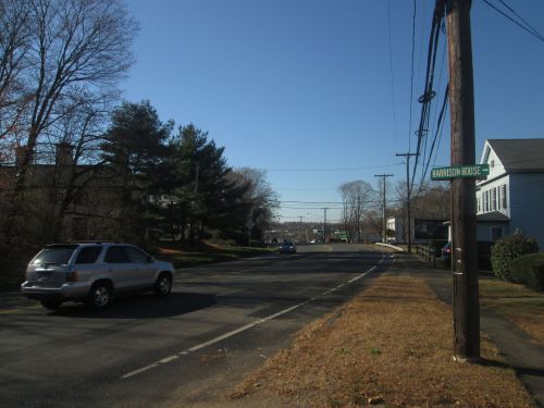 A quiet street scene with a car, power lines, and a sign for "Harrison House" under a clear blue sky.
