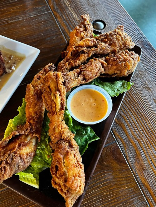 A platter of crispy fried chicken wings served on lettuce with a small cup of dipping sauce.