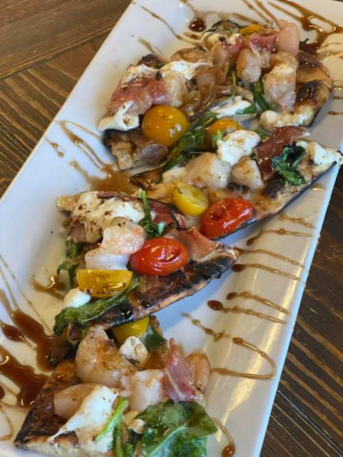 Three grilled flatbreads topped with shrimp, cherry tomatoes, greens, and drizzled with balsamic glaze.