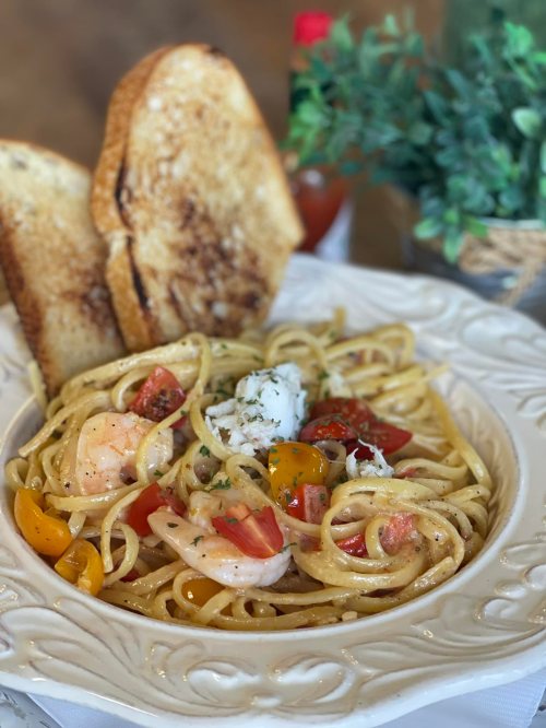 A plate of shrimp pasta with tomatoes, topped with herbs, served with two slices of toasted bread and a small plant in the background.