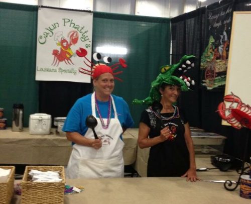 Two people in colorful hats pose at a booth with a Cajun theme, featuring crab and alligator decorations.