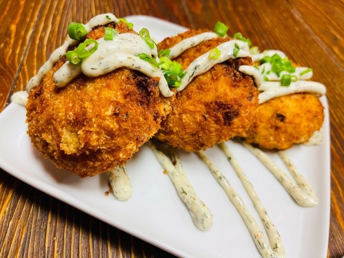 Three golden-brown fried balls drizzled with creamy sauce and topped with green onions, served on a white plate.
