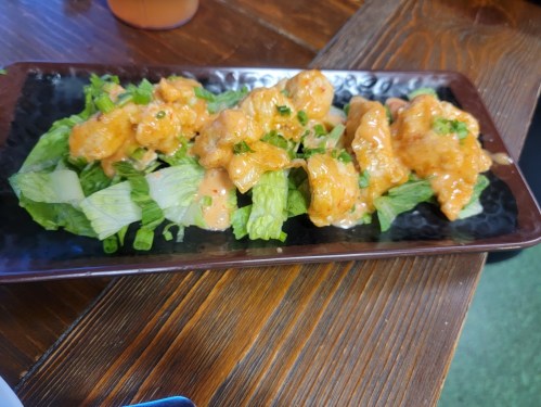 A plate of crispy chicken pieces on a bed of lettuce, drizzled with a creamy sauce.