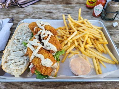 A tray with a fried chicken sandwich topped with sauce, lettuce, and tomato, alongside a serving of crispy fries.