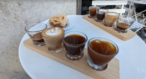 A wooden tray with various coffee drinks and a cinnamon roll on a table.
