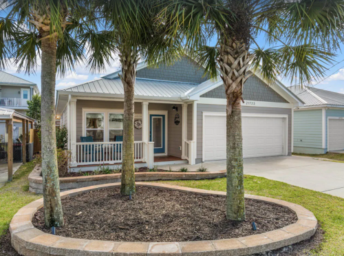 A charming house with a porch, surrounded by palm trees and a landscaped garden, featuring a driveway and garage.