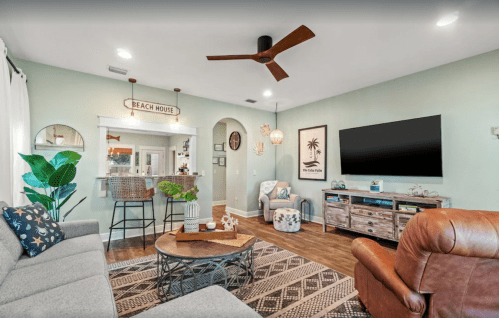 Cozy living room with a beach house theme, featuring a fan, plants, and stylish furniture in soft colors.
