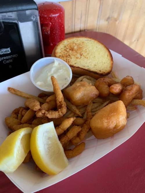 A plate of fried seafood, including shrimp and fish, served with lemon wedges, a side of tartar sauce, and toasted bread.