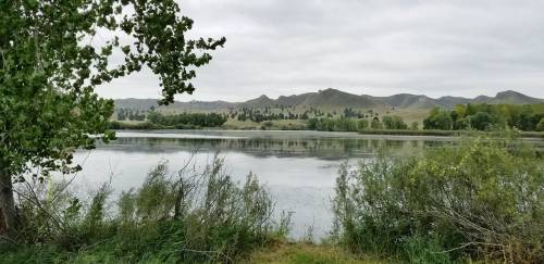 A serene lake surrounded by lush greenery and distant mountains under a cloudy sky.