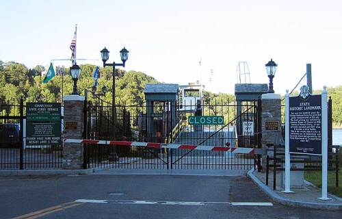A closed gate at a historic site, with signs indicating closure and information about the location.
