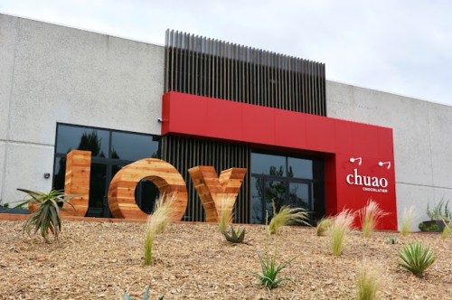 Exterior of Chuao Chocolatier with large wooden letters spelling "JOY" and modern architecture.