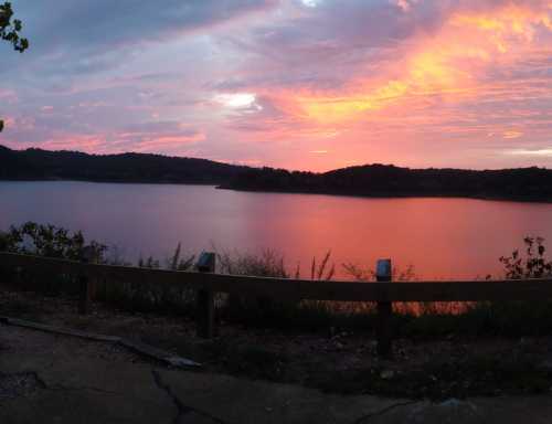 A serene lake at sunset, with vibrant pink and orange hues reflecting on the water and hills in the background.