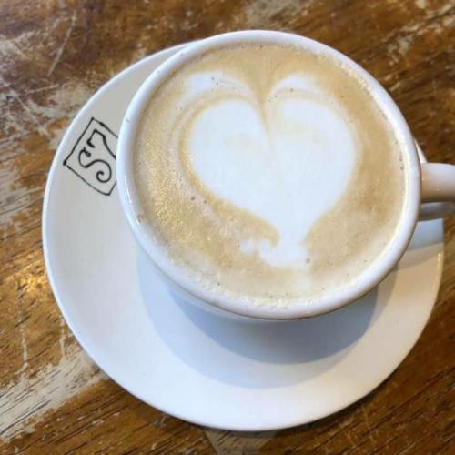 A cup of latte with a heart-shaped foam design, sitting on a white saucer on a wooden table.