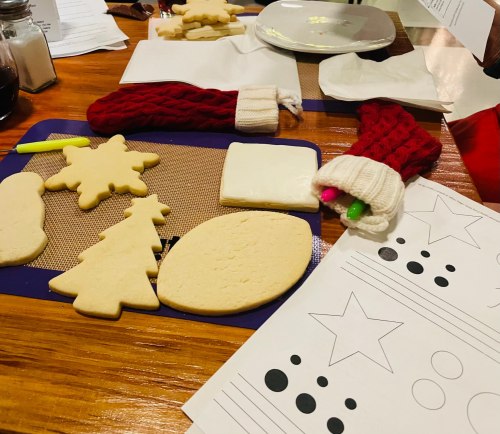 A table with decorated cookies, holiday-themed shapes, and colorful markers, ready for a festive baking activity.
