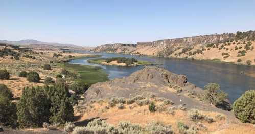 A scenic view of a river winding through arid hills and greenery under a clear blue sky.