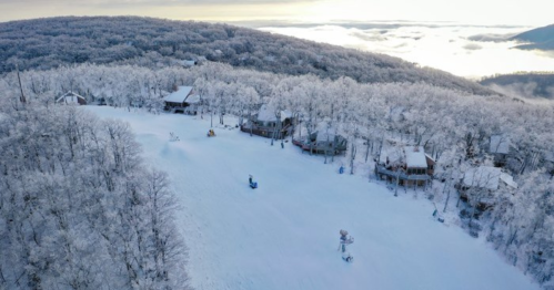 Aerial view of a snowy landscape with cabins nestled among frosted trees and a misty valley below.
