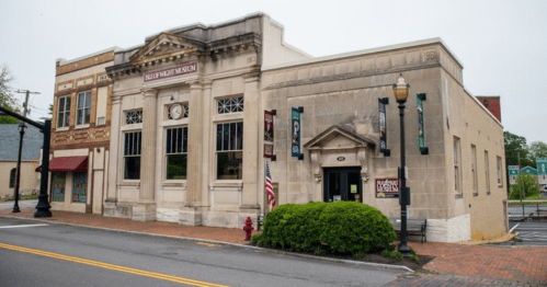 Historic building of the museum with large windows, clock, and American flag, surrounded by greenery and brick pavement.
