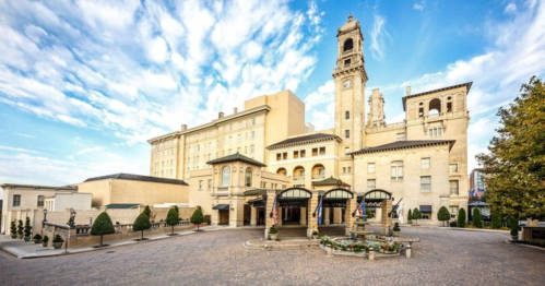 Historic building with a clock tower, surrounded by manicured gardens and a clear blue sky.
