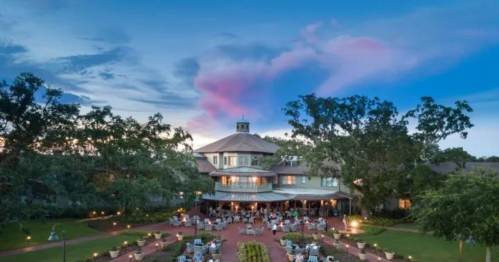 A scenic view of a resort with outdoor seating, surrounded by trees and a colorful sky at dusk.