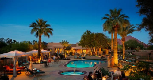 A serene resort scene at dusk, featuring a pool, palm trees, and cozy seating areas with warm lighting.