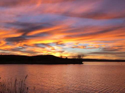A serene lake at sunset, with vibrant orange and purple clouds reflecting on the water's surface.