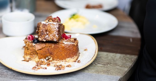 A plate with two pieces of cake topped with berries and powdered sugar, with a blurred background of another dish.
