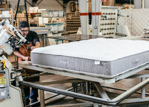 A worker operates machinery to assemble a mattress in a manufacturing facility.
