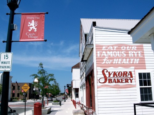 A street view of Czech Village featuring a bakery sign and a parking sign under a clear blue sky.