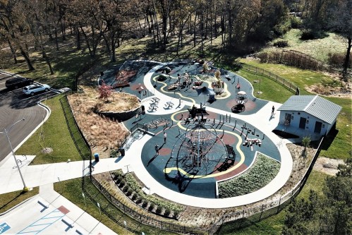 Aerial view of a colorful playground with various play structures, surrounded by green grass and trees.