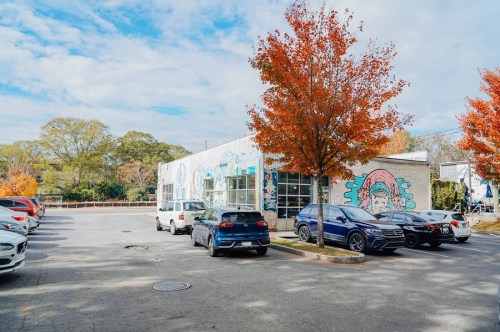 A parking lot with several cars and a colorful mural on a building, surrounded by autumn trees with orange leaves.