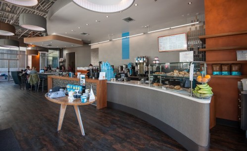 A modern café interior featuring a coffee counter, pastries, and seating areas with customers enjoying their time.