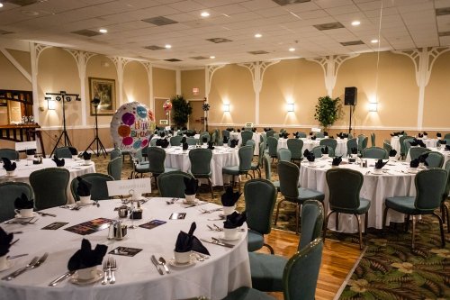 A banquet hall set up with round tables, green chairs, and elegant table settings, ready for an event.