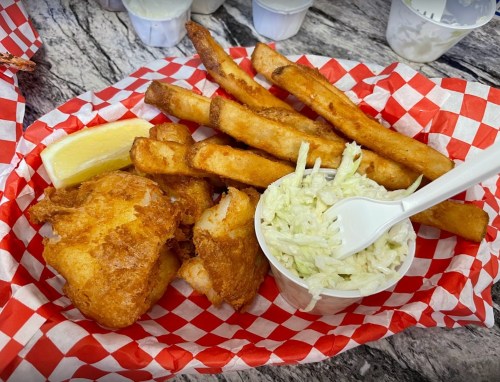 A basket of fried fish, golden fries, and coleslaw on a red and white checkered paper. A lemon wedge is included.