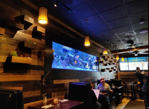 A cozy restaurant interior featuring a large aquarium, wooden walls, and dim lighting with patrons seated at tables.