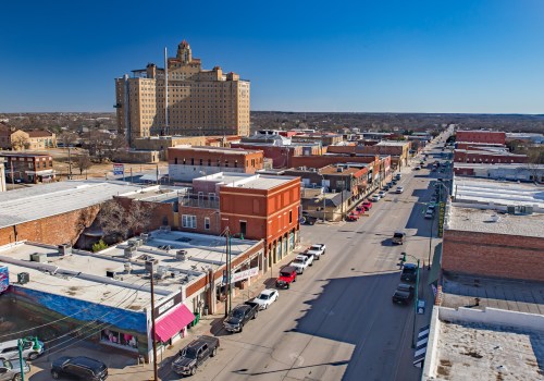 Aerial view of a small town street lined with shops and cars, featuring a large historic building in the background.